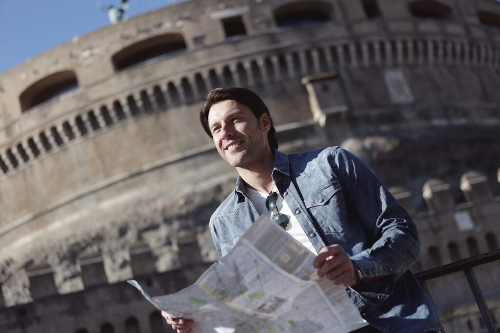 A young man holding a map smiles in front of Castle Sant'Angelo in Rome, Italy.